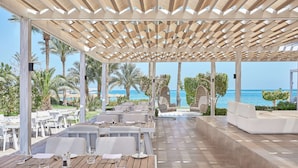An outdoor dining area with wooden tables and white chairs, overlooking the sea. - Steigenberger ALDAU Beach Hotel (Hurghada)