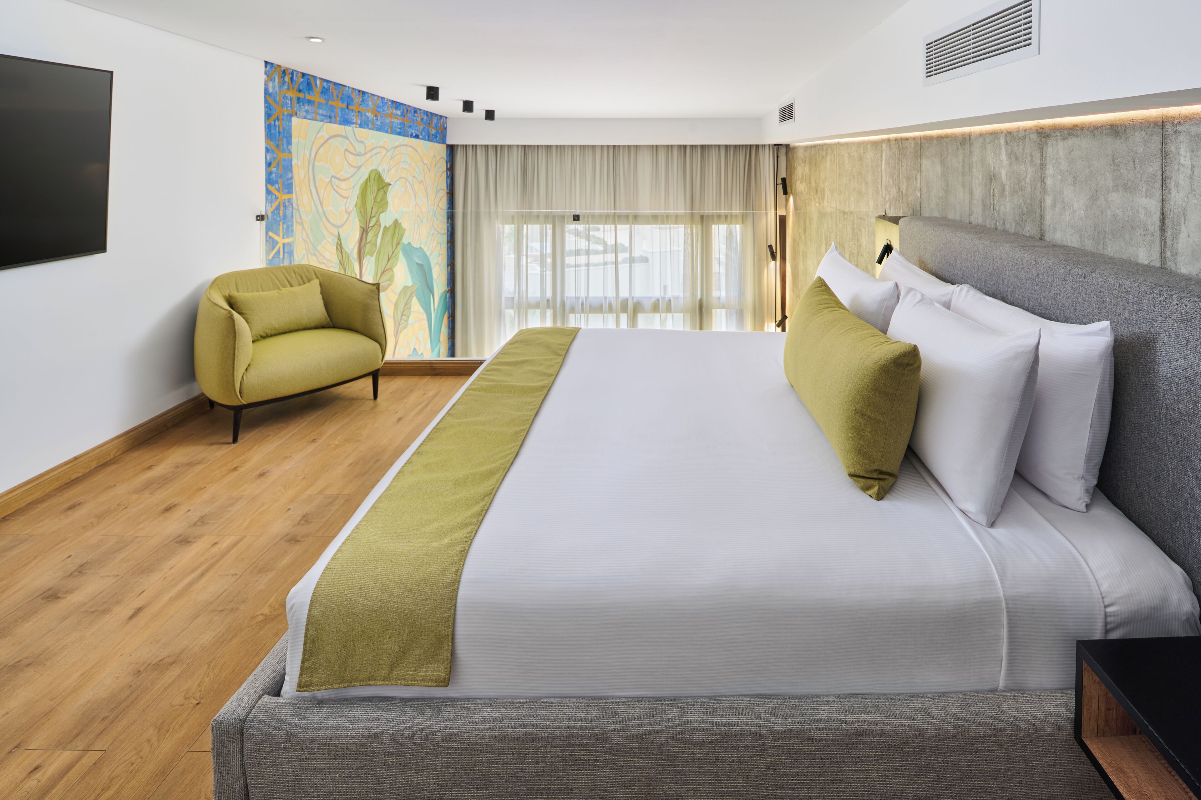 Una habitación de hotel moderna con una cama grande, un sofá, un televisor y un mural en la pared.