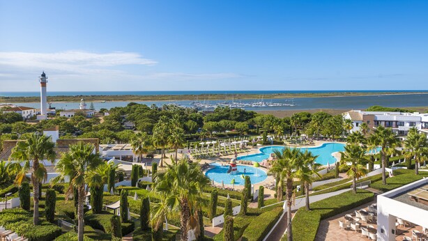 A resort with a large swimming pool, palm trees, and a lighthouse in the background.