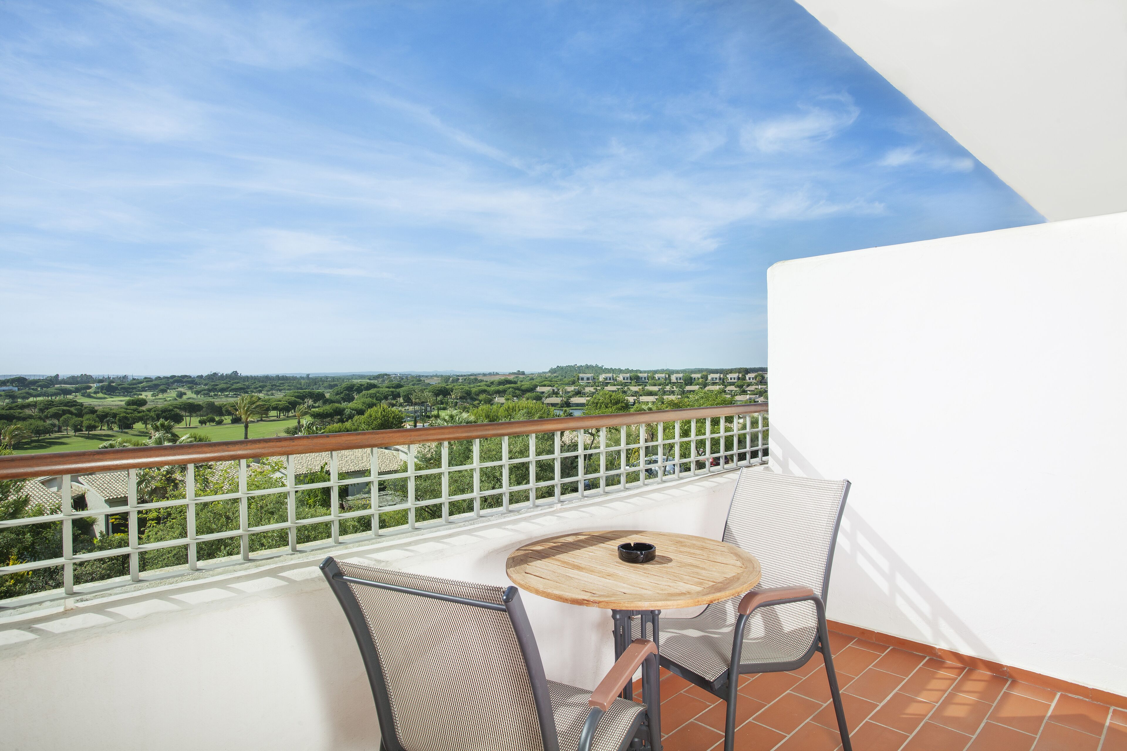 Un balcon donnant sur un paysage verdoyant, une table ronde en bois et deux chaises.