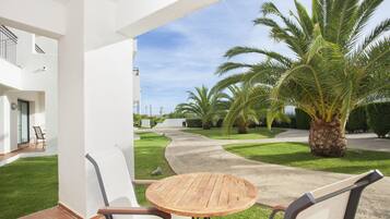 Un espacio al aire libre cubierto con una mesa redonda de madera y dos sillas, un sendero empedrado y varias palmeras.