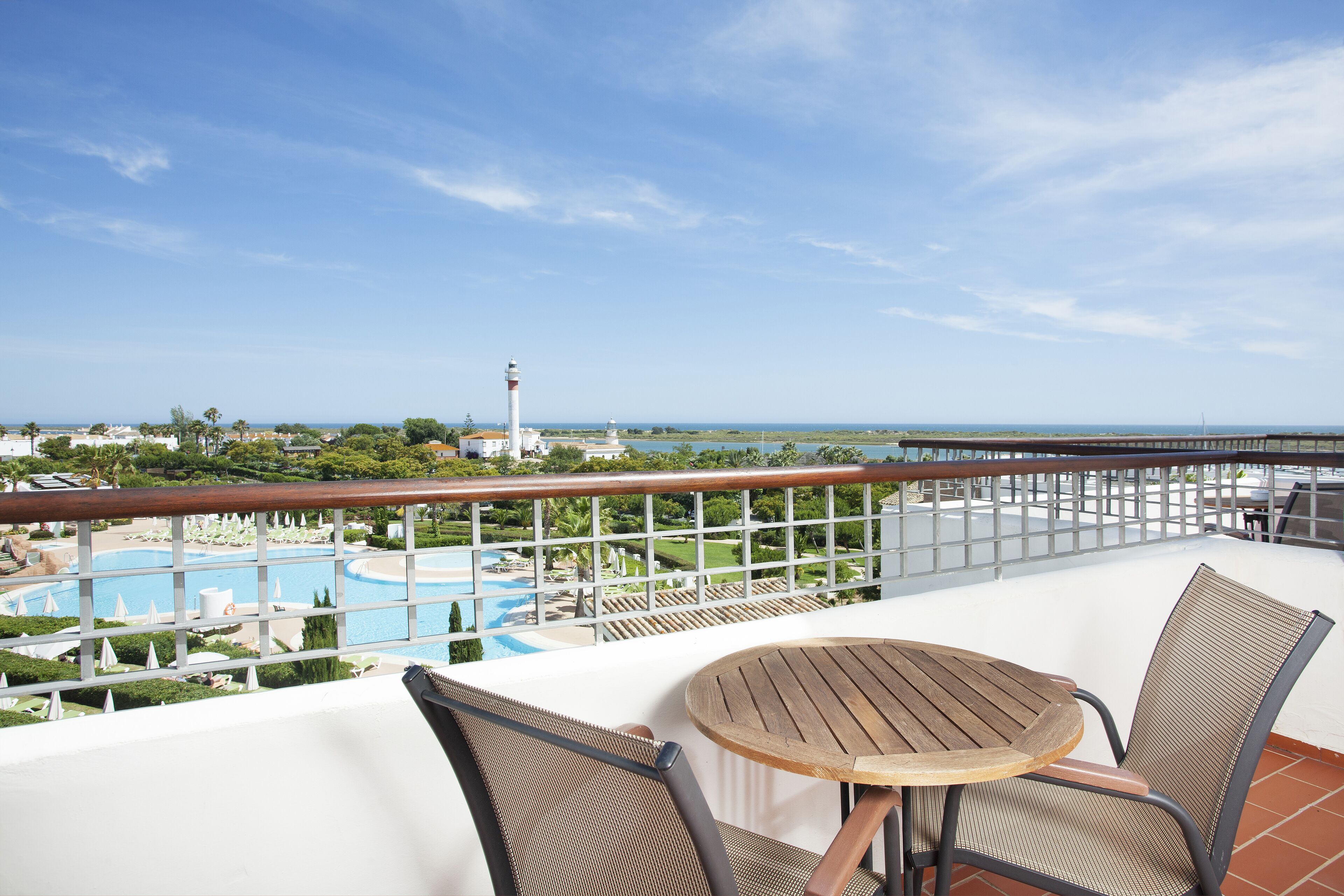 A balcony with a table and chairs overlooking a pool and a lighthouse.