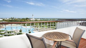 A balcony with a table and chairs overlooking a pool and a lighthouse.
