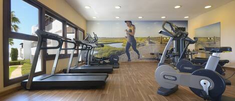 Een sportschool met loopbanden, een hometrainer en een muurschildering van een hardloper.