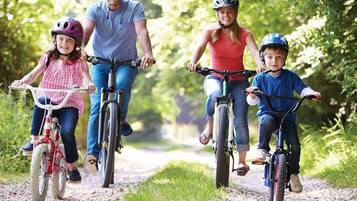 Una familia pasea en bicicleta por un camino de grava rodeado de vegetación.