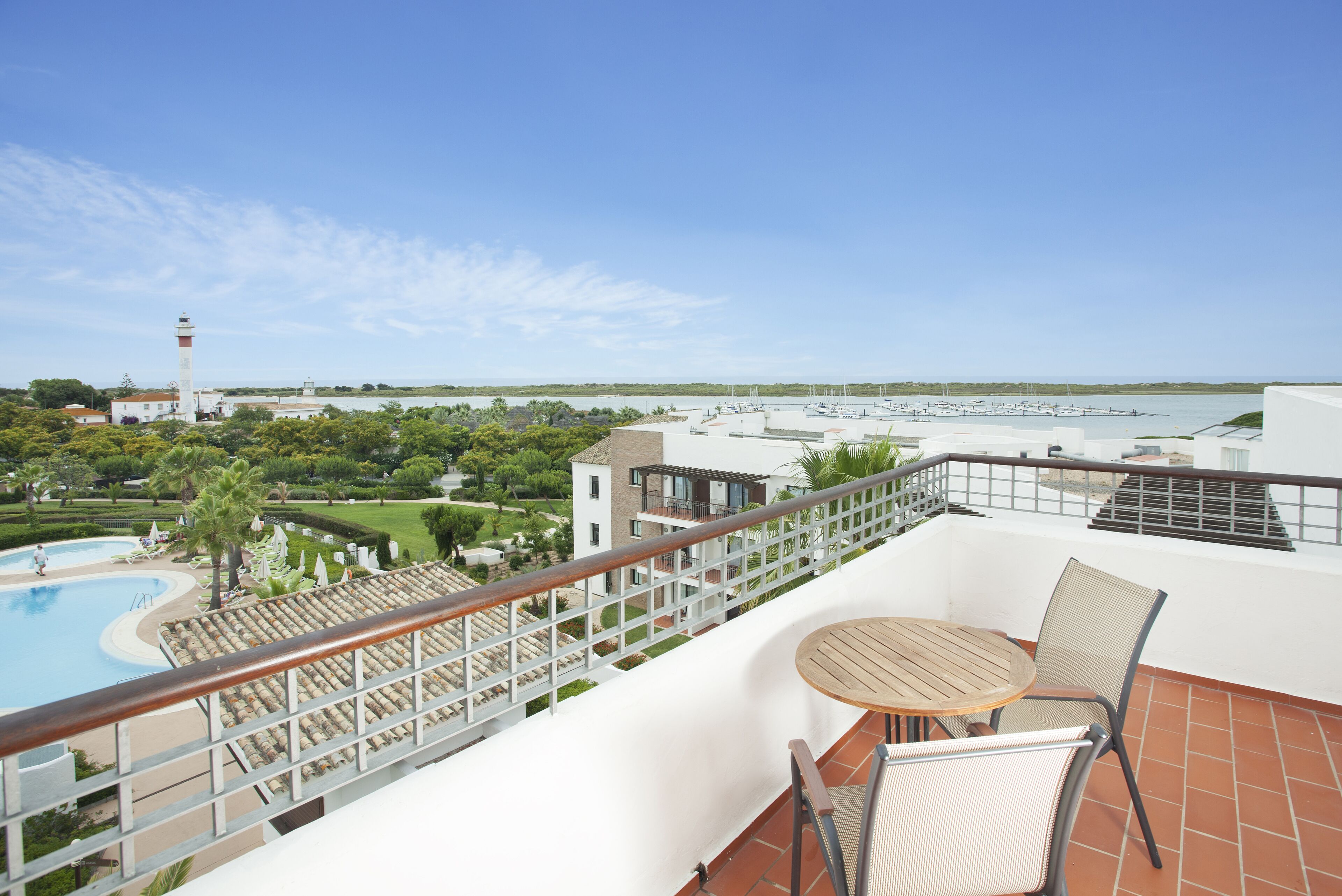 Un balcon avec vue sur une piscine, un phare et un port de plaisance.