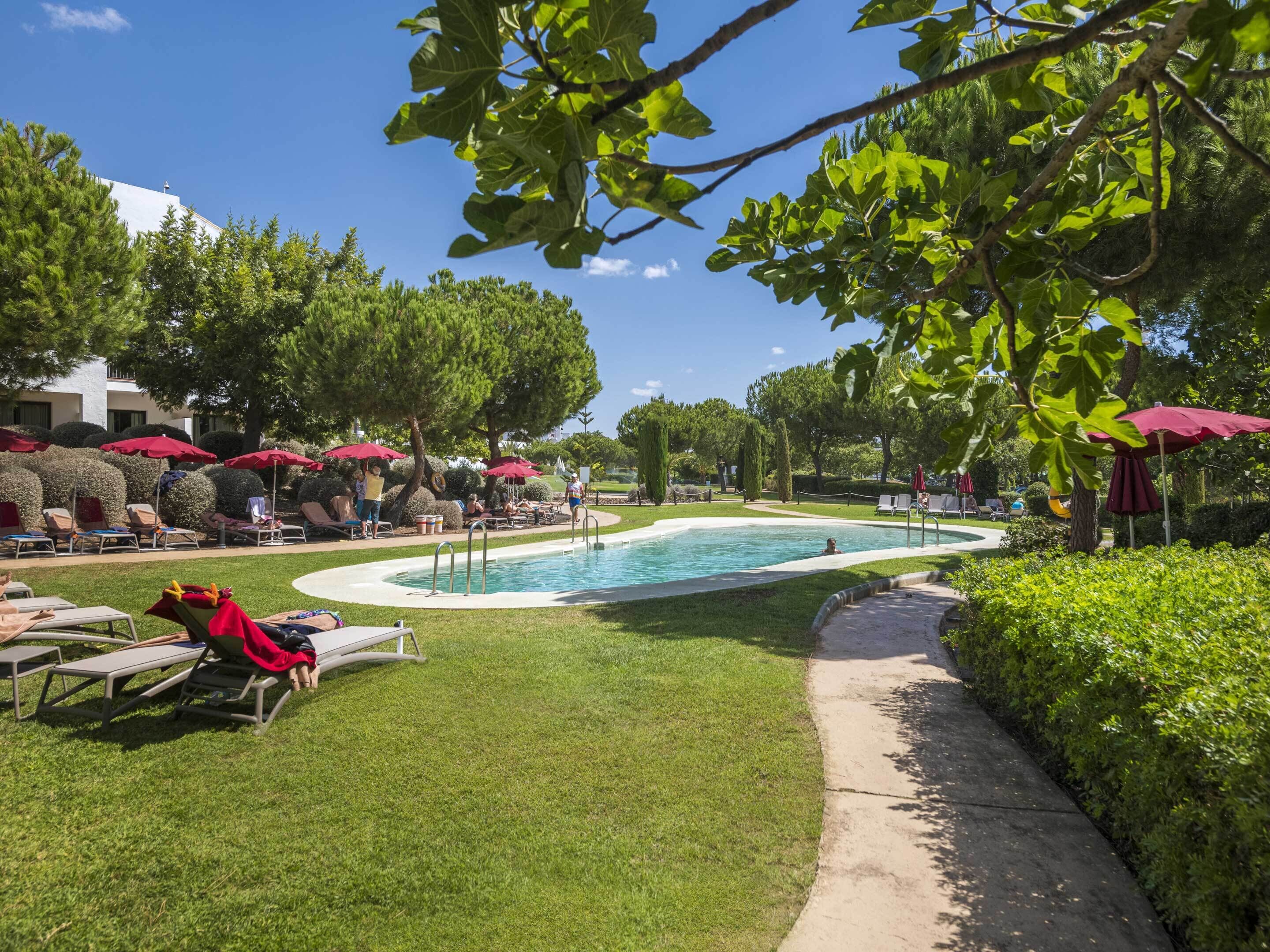 A pool area with lounge chairs and umbrellas, surrounded by greenery and trees.