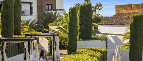 Un jardín con una cama, una pérgola y un edificio al fondo.