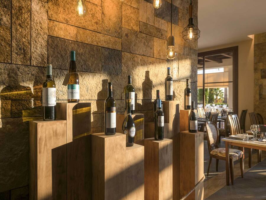 A wine tasting room with wooden counters displaying various wine bottles, a stone wall, and hanging light fixtures.