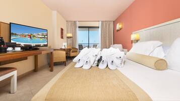 Habitación de hotel con cama, escritorio con televisor, silla y vista a una piscina y edificios.