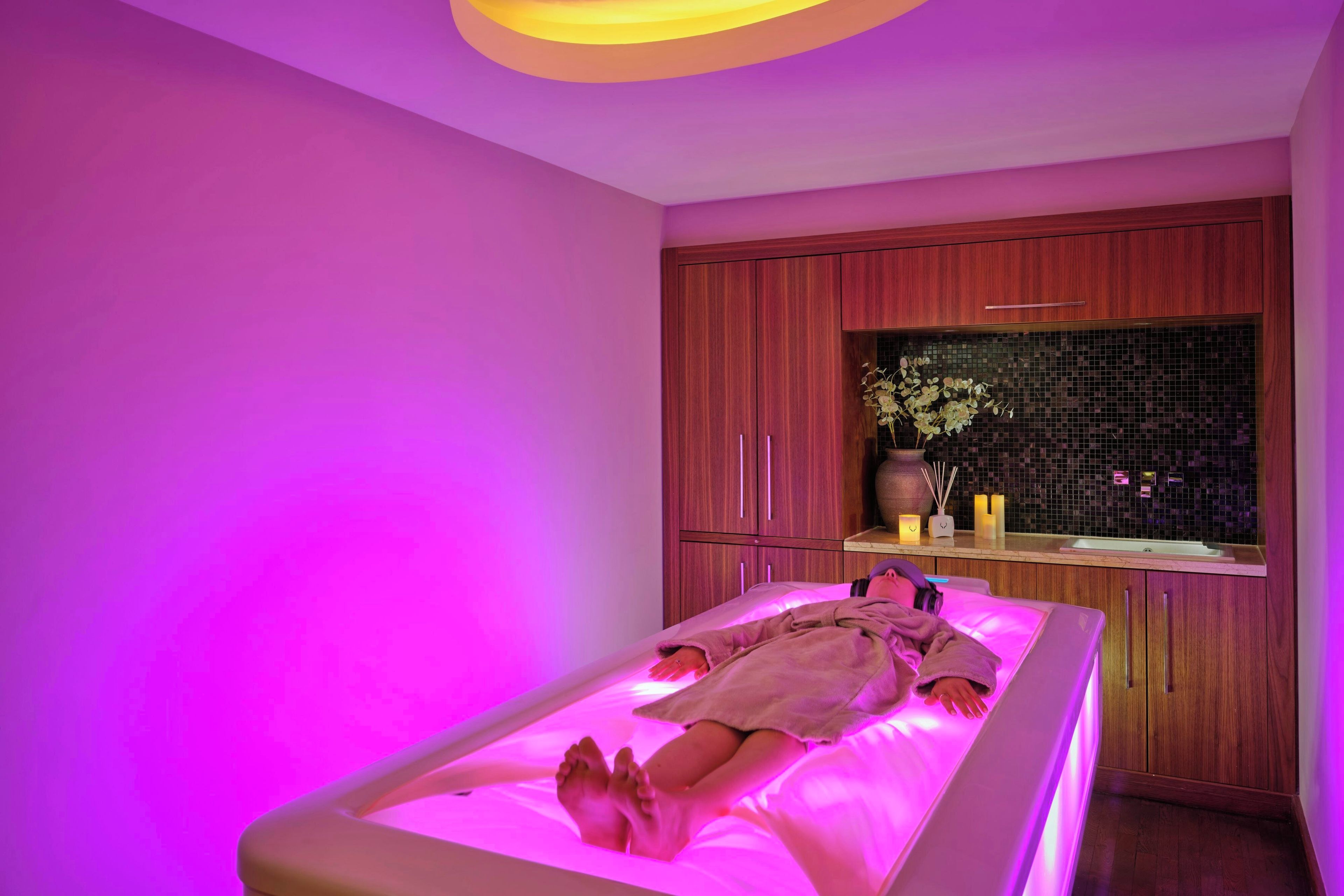 A massage therapy room with a single bed, wooden cabinets, and a decorative vase.