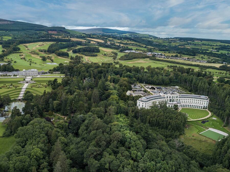 Un edificio grande e histórico con una distribución simétrica, rodeado de abundante vegetación y un campo de golf bien cuidado.