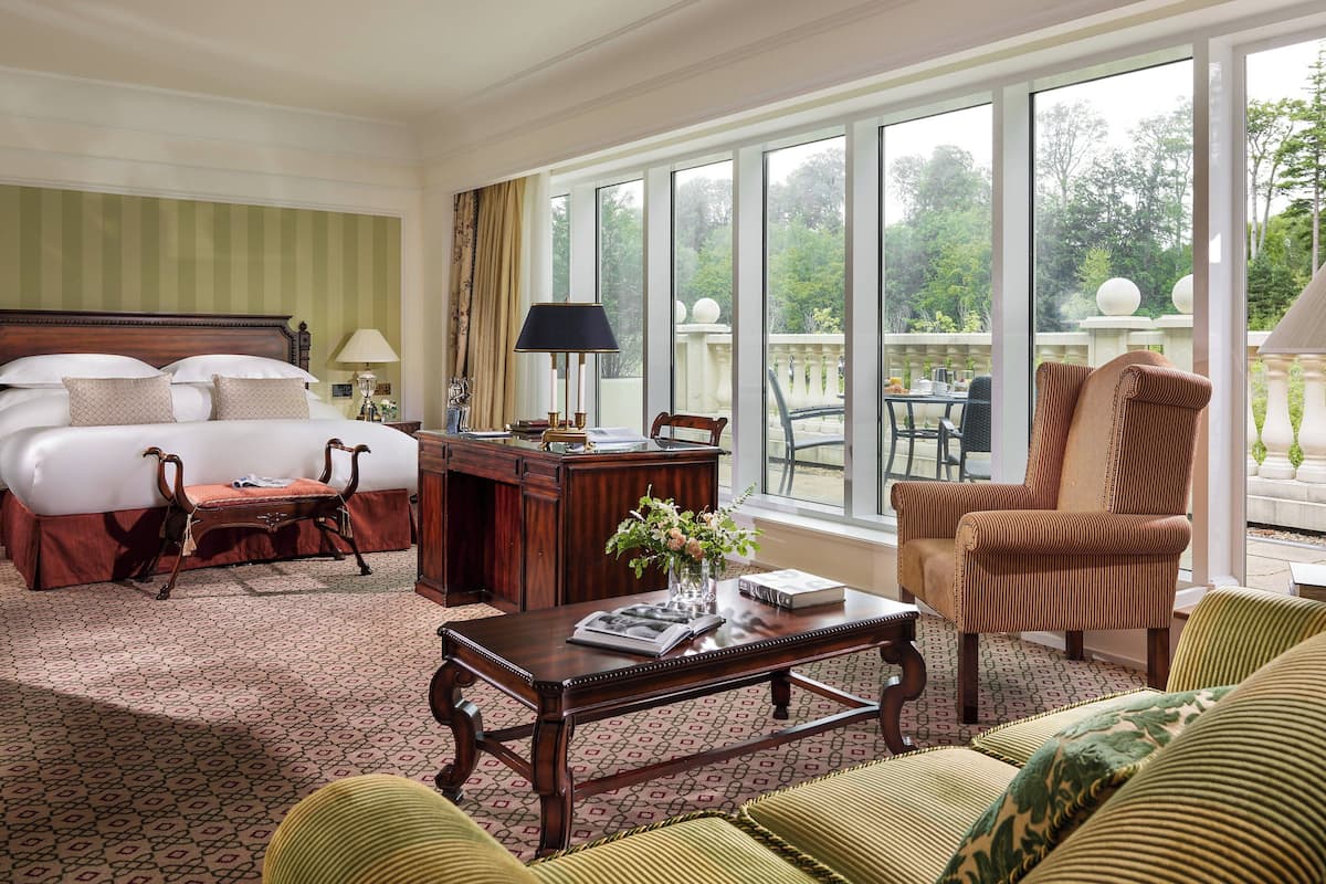 Une chambre d’hôtel dotée d’un grand lit, d’un coin salon avec un canapé et des fauteuils, d’une table à manger et d’un balcon offrant une vue sur la verdure.