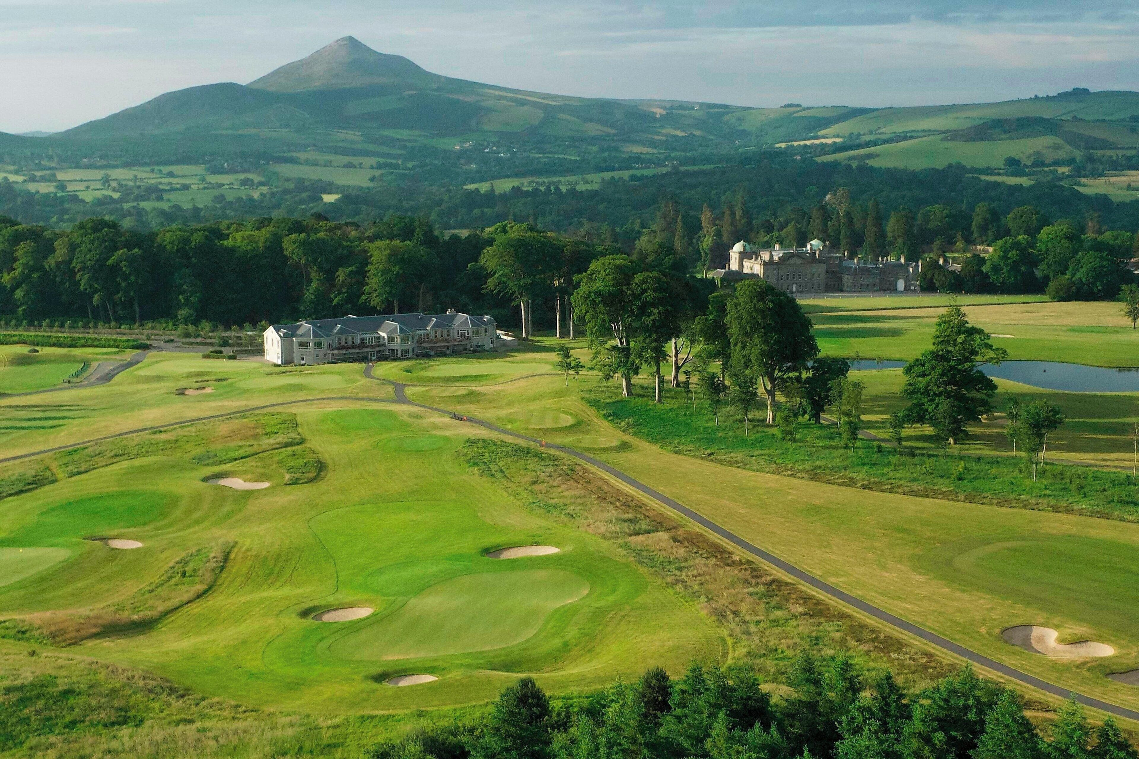 A golf course with a clubhouse, a pond, and a mountain in the background.