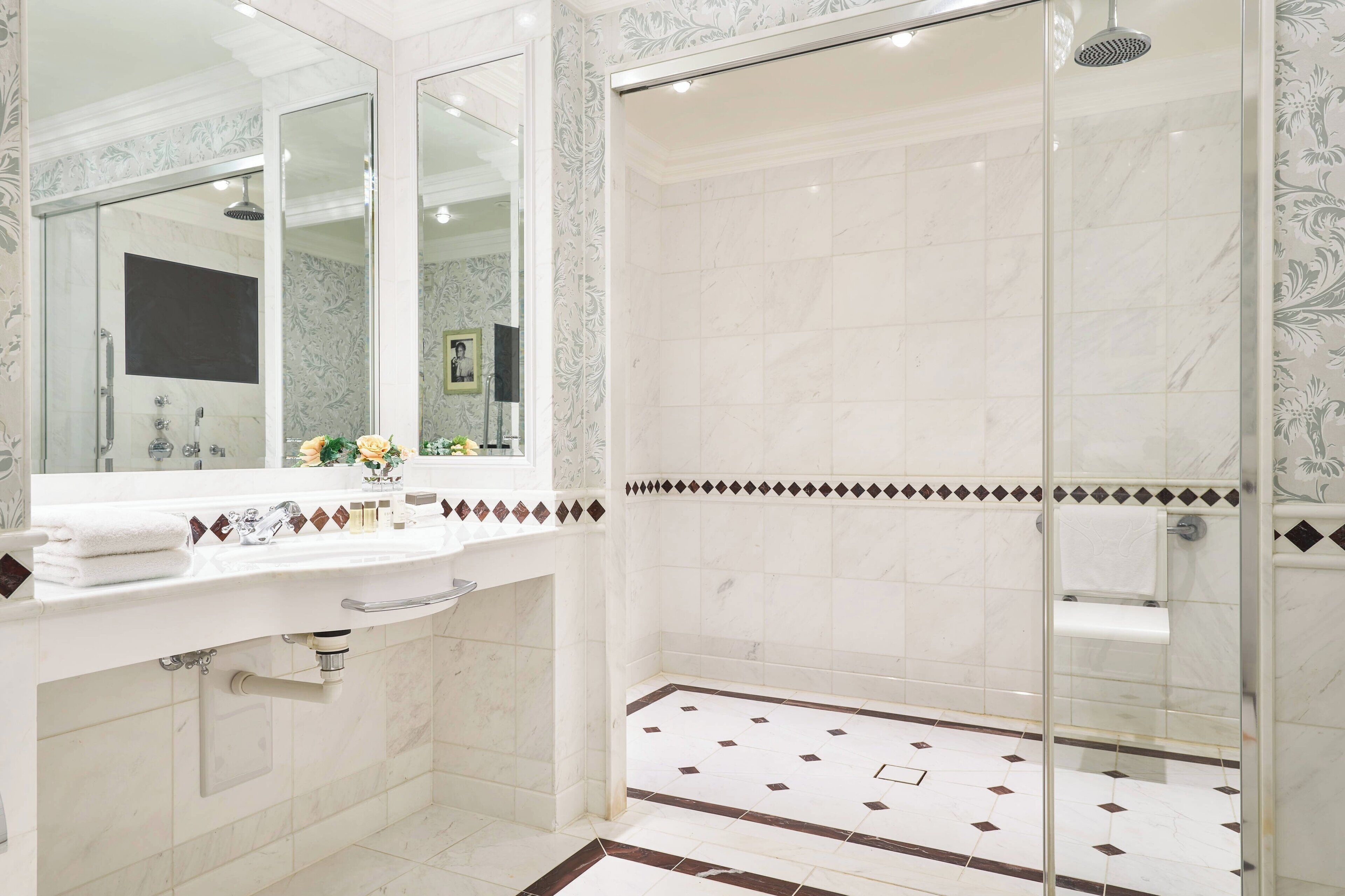 Une salle de bain avec un grand miroir, un lavabo avec une serviette et un espace douche.