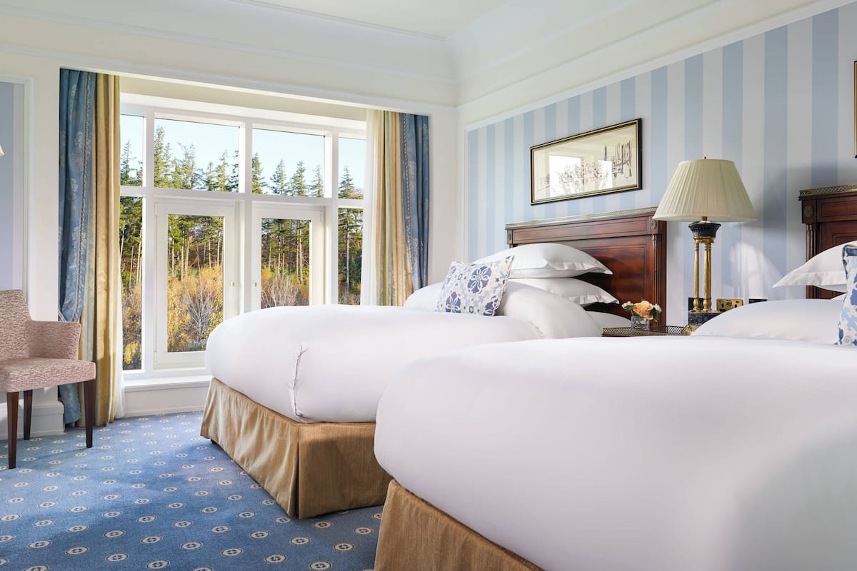 Une chambre d’hôtel avec deux lits, une chaise, une lampe et une fenêtre avec des rideaux.