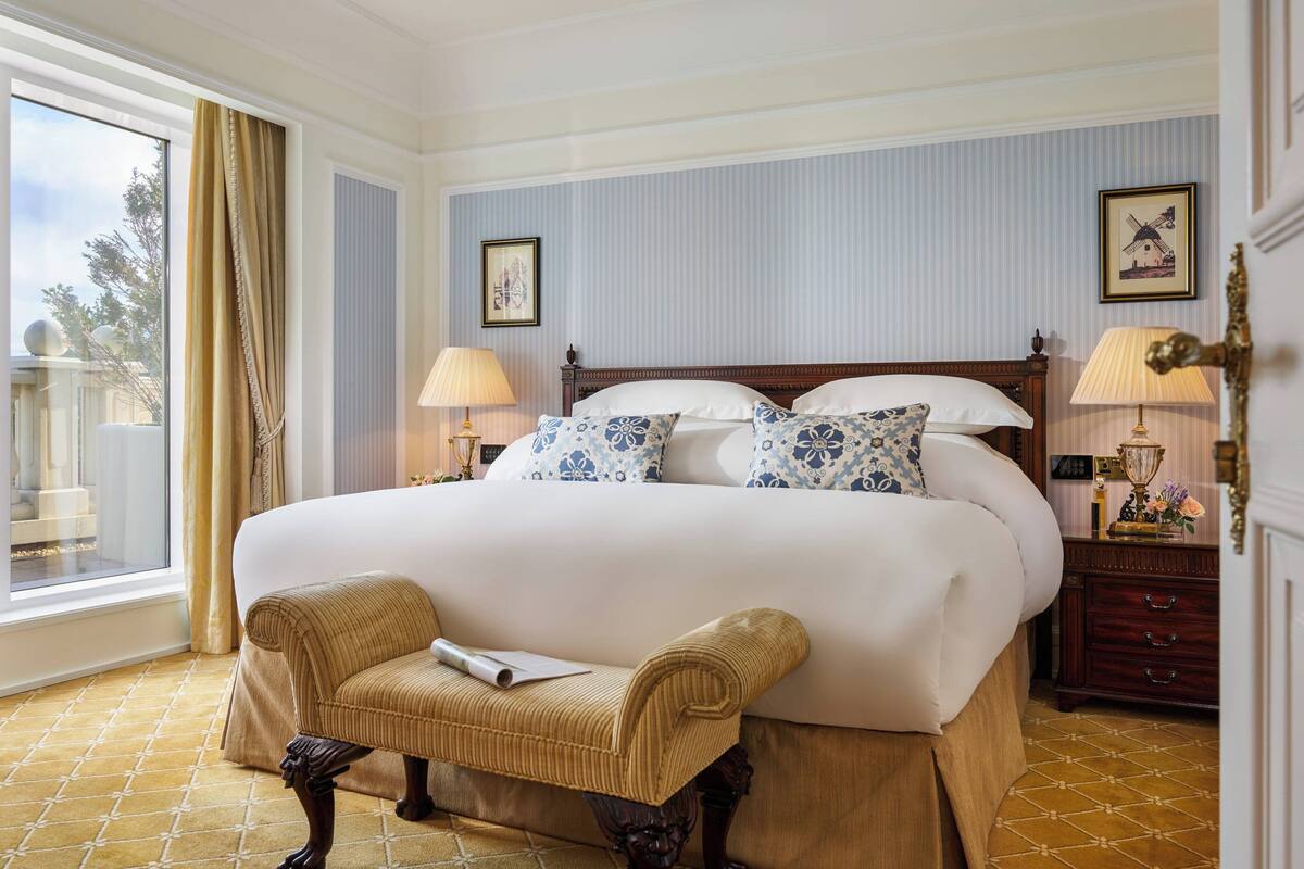 Une chambre d’hôtel avec un grand lit, deux lampes de chevet, une chaise et une fenêtre avec des rideaux.