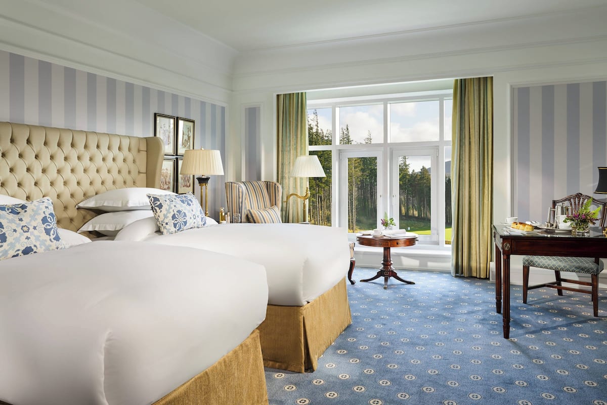 Une chambre d’hôtel avec deux grands lits, une petite table, une chaise et une vue sur l’extérieur.