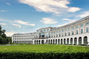 Un edificio grande de estilo clásico con fachada simétrica, múltiples ventanas y un patio central con una fuente.