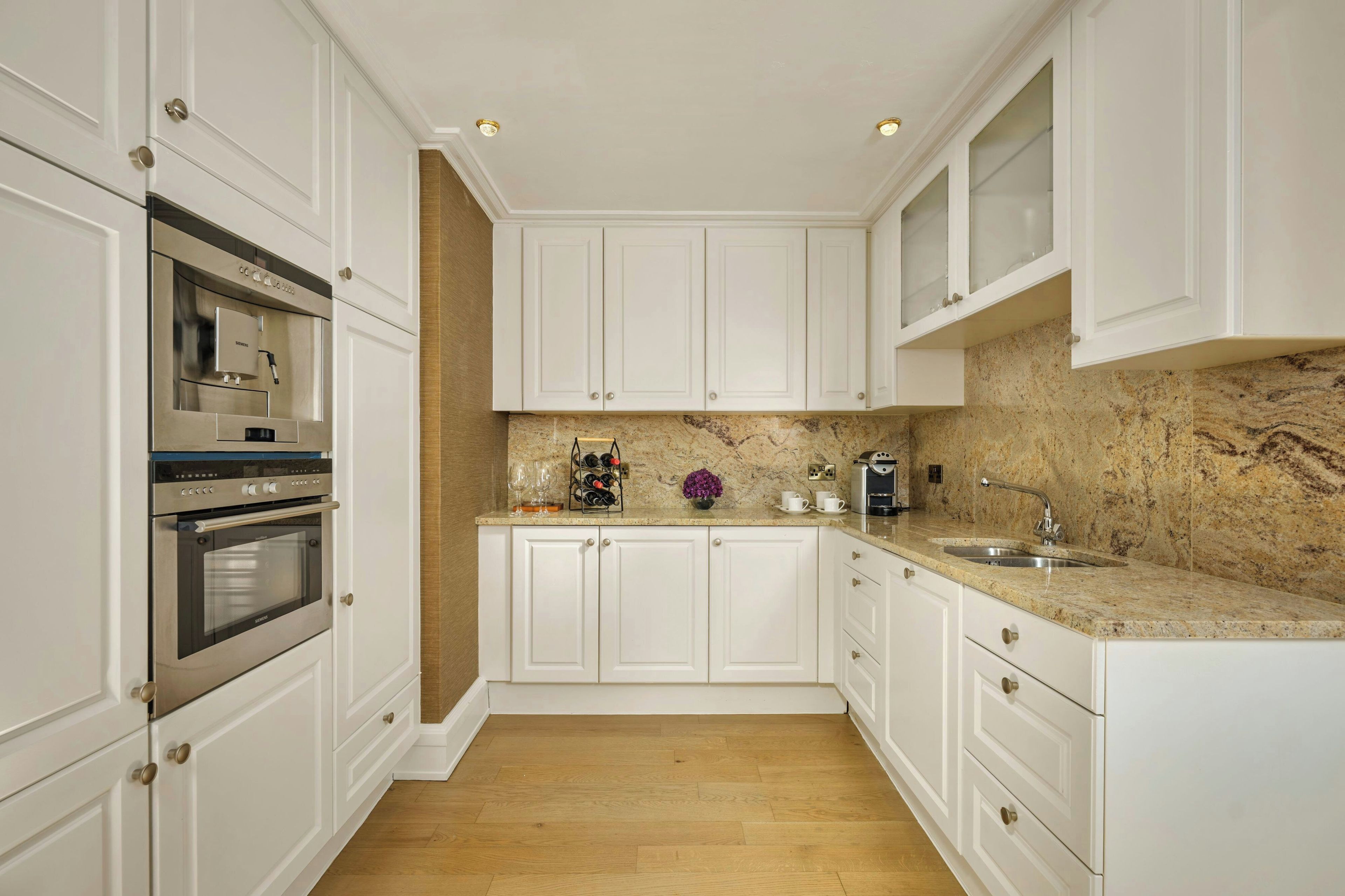 A modern kitchen with white cabinetry, stainless steel appliances, a marble countertop, and a wooden floor.