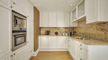 A modern kitchen with white cabinetry, stainless steel appliances, a marble countertop, and a wooden floor.