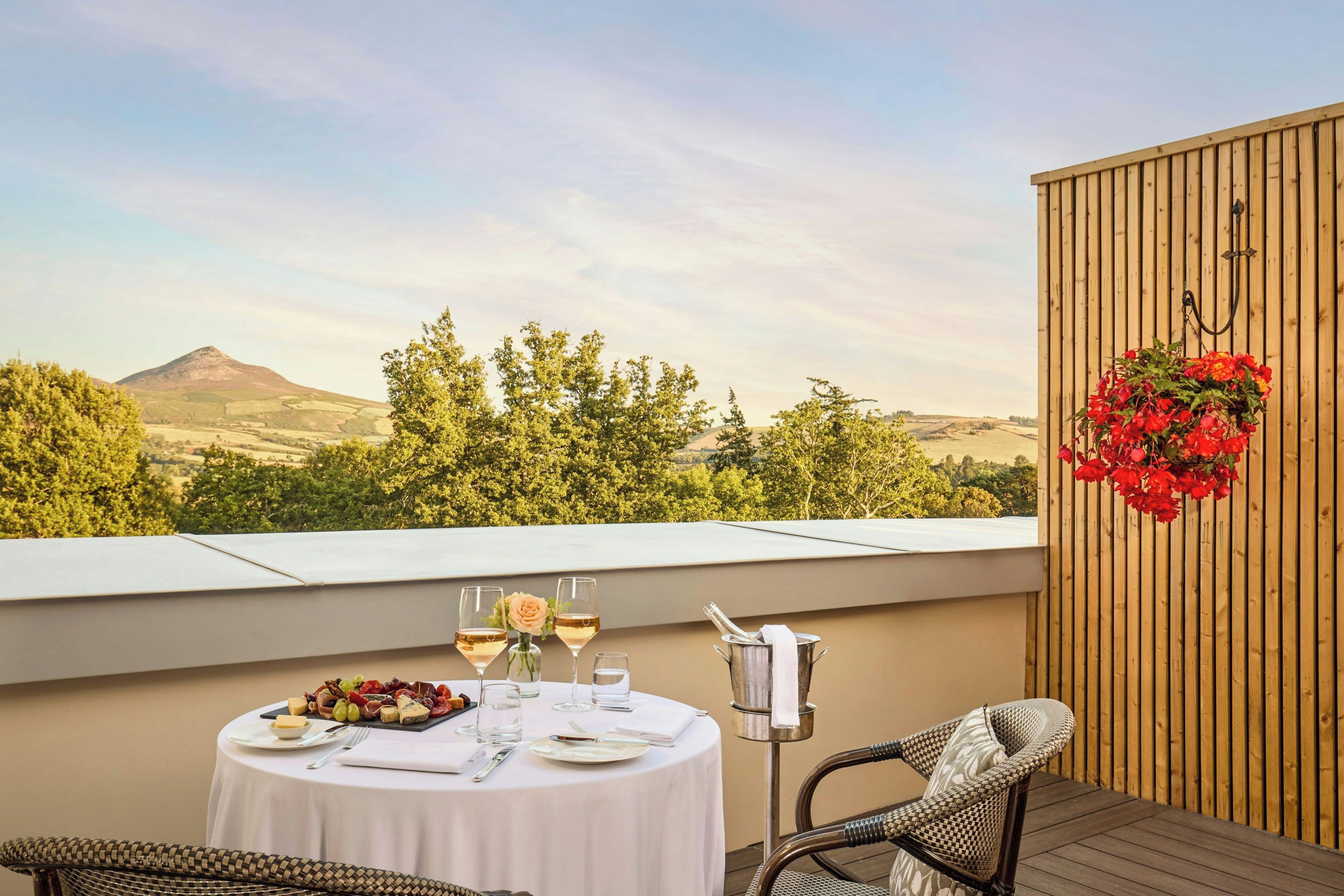 A terrace with a table set for two, featuring a wine glass, a bottle, and a fruit platter.