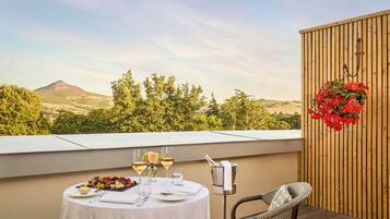 A terrace with a table set for two, featuring a wine glass, a bottle, and a fruit platter.
