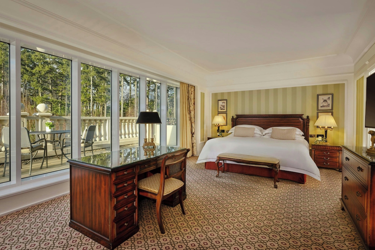 Een hotelkamer met een groot bed, een bureau en uitzicht op de omgeving door grote ramen.