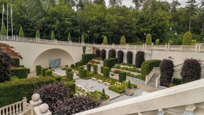 A formal garden with a bridge, neatly trimmed hedges, and a fountain.