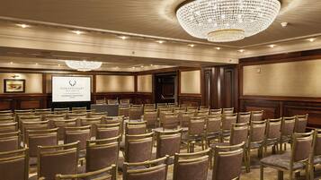 A conference room with rows of chairs, a projector screen, and a chandelier.