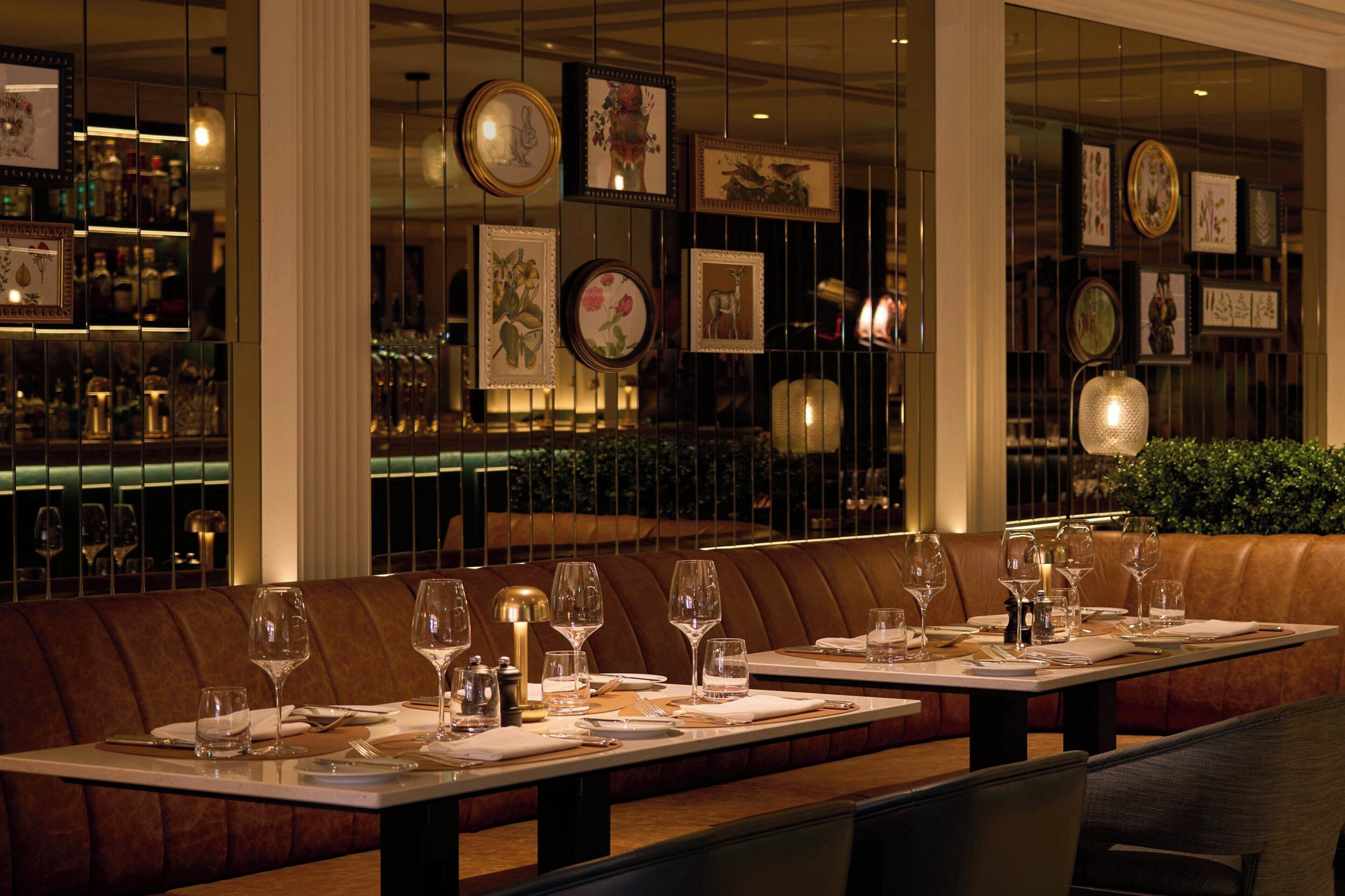 A restaurant with a long table set for dining, a bar area with bottles, and framed pictures on the walls.