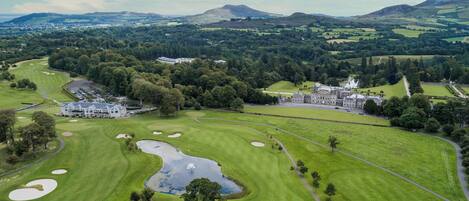 A golf course with a clubhouse, a pond, and surrounding hills.