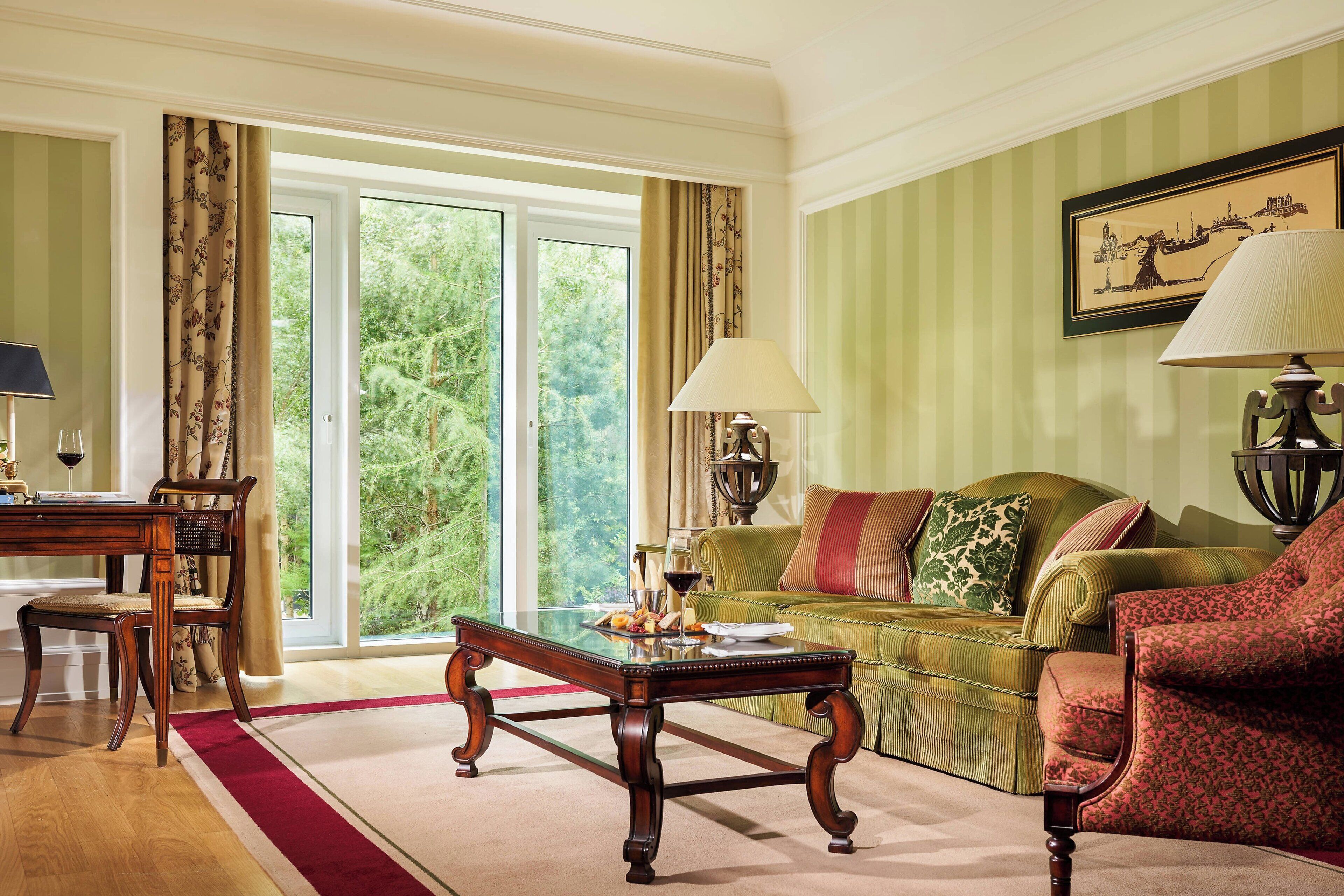 Un salon bien éclairé, avec une table basse en bois, un canapé et un fauteuil. Une grande fenêtre offre une vue sur la verdure à l’extérieur.