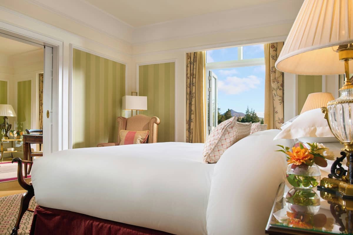 Une chambre d’hôtel avec un grand lit, une chaise, une table avec une lampe et une vue sur l’extérieur.