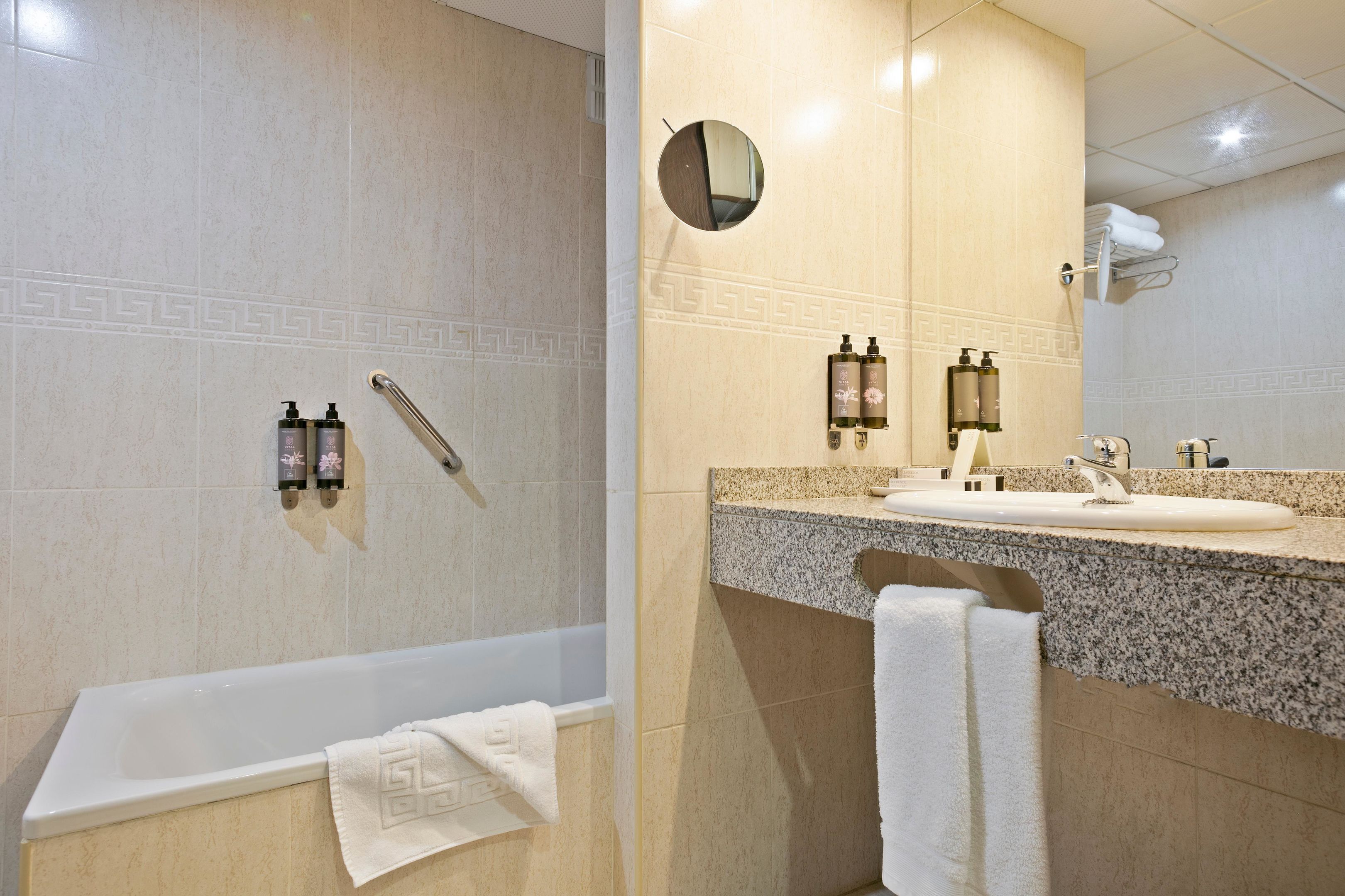 Un baño moderno con bañera, lavabo con encimera de granito y espejo con marco redondo.