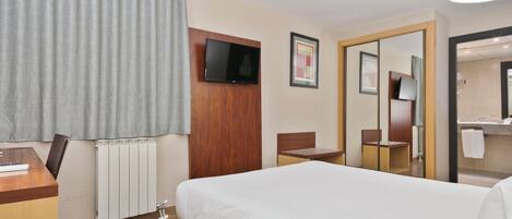 Habitación de hotel con cama, escritorio, silla, televisión y baño visible a través de una puerta abierta.