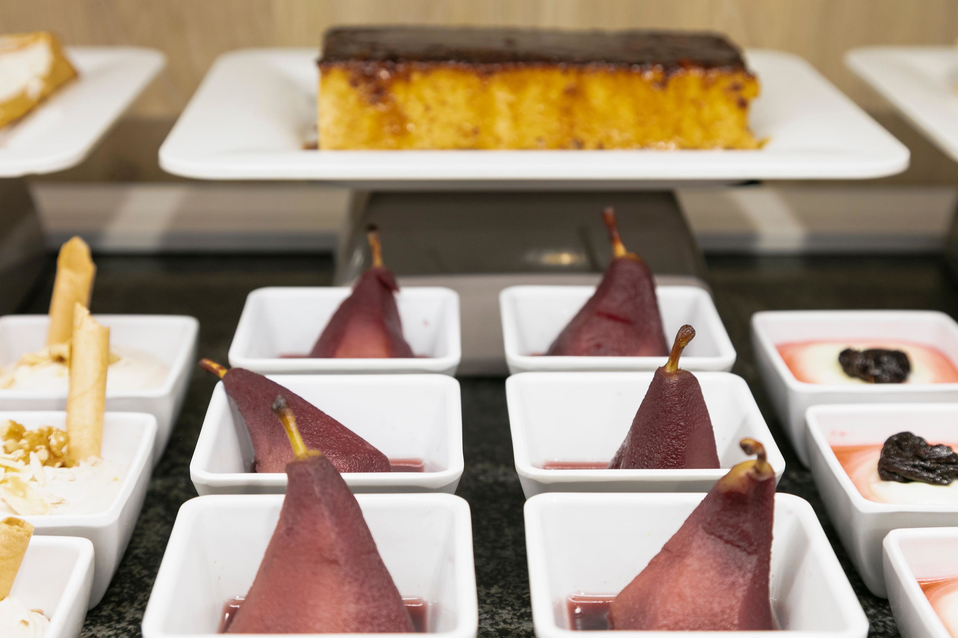 Una exhibición de postres con diversos dulces en recipientes blancos, incluyendo una rebanada de pastel sobre un plato blanco al fondo.