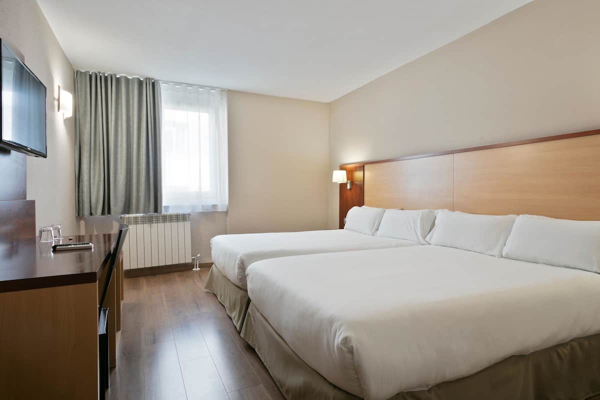 Una habitación de hotel con dos camas, un escritorio, un televisor y una ventana con cortinas.