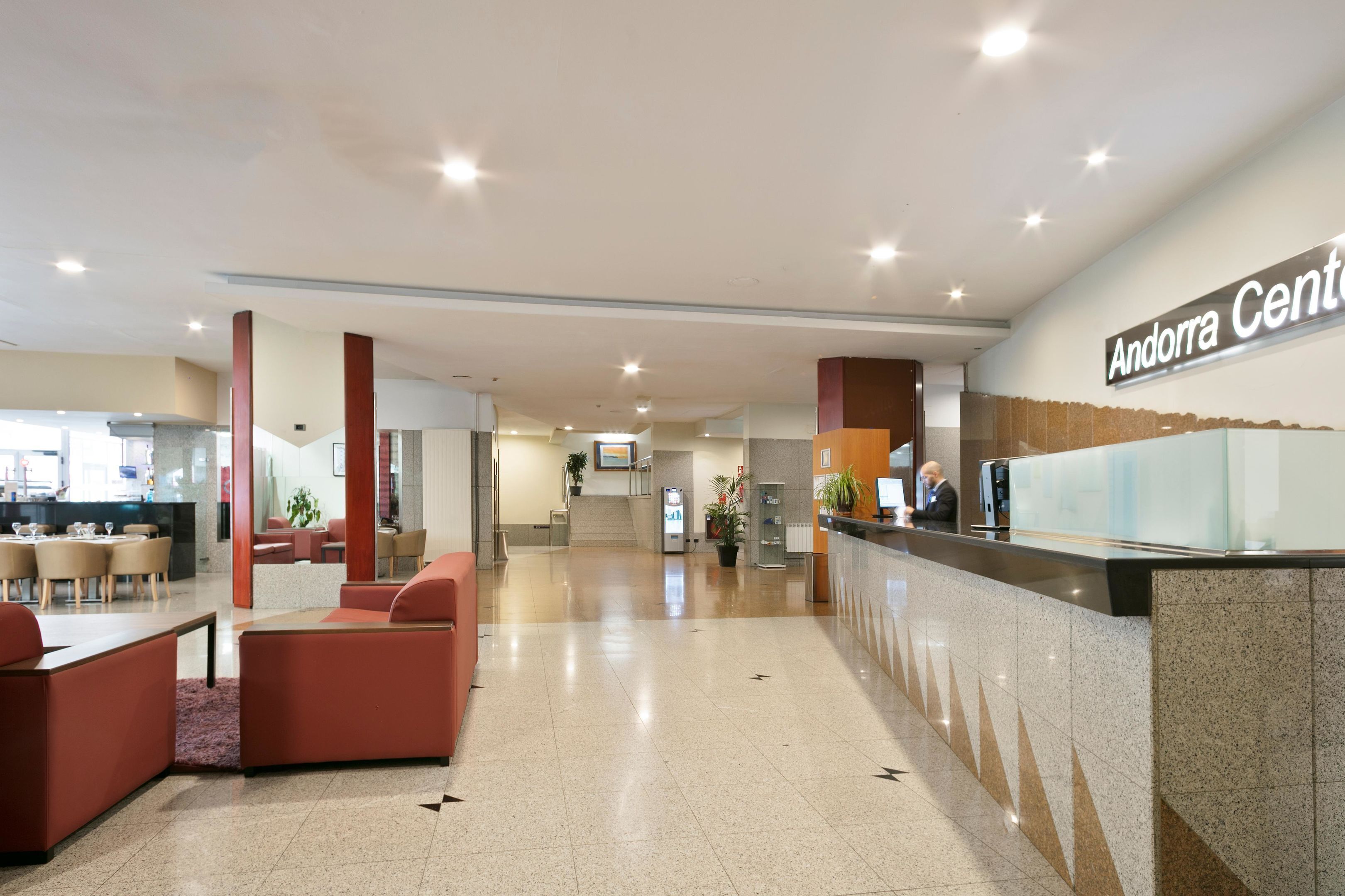Un moderno hall de hotel con mostrador de recepción, zona de estar y una escalera que conduce a los pisos superiores.