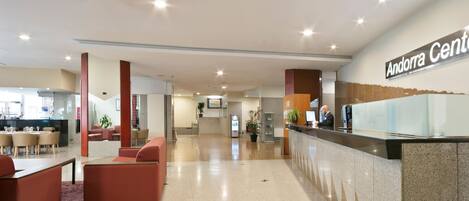 Un moderno hall de hotel con mostrador de recepción, zona de estar y una escalera que conduce a los pisos superiores.