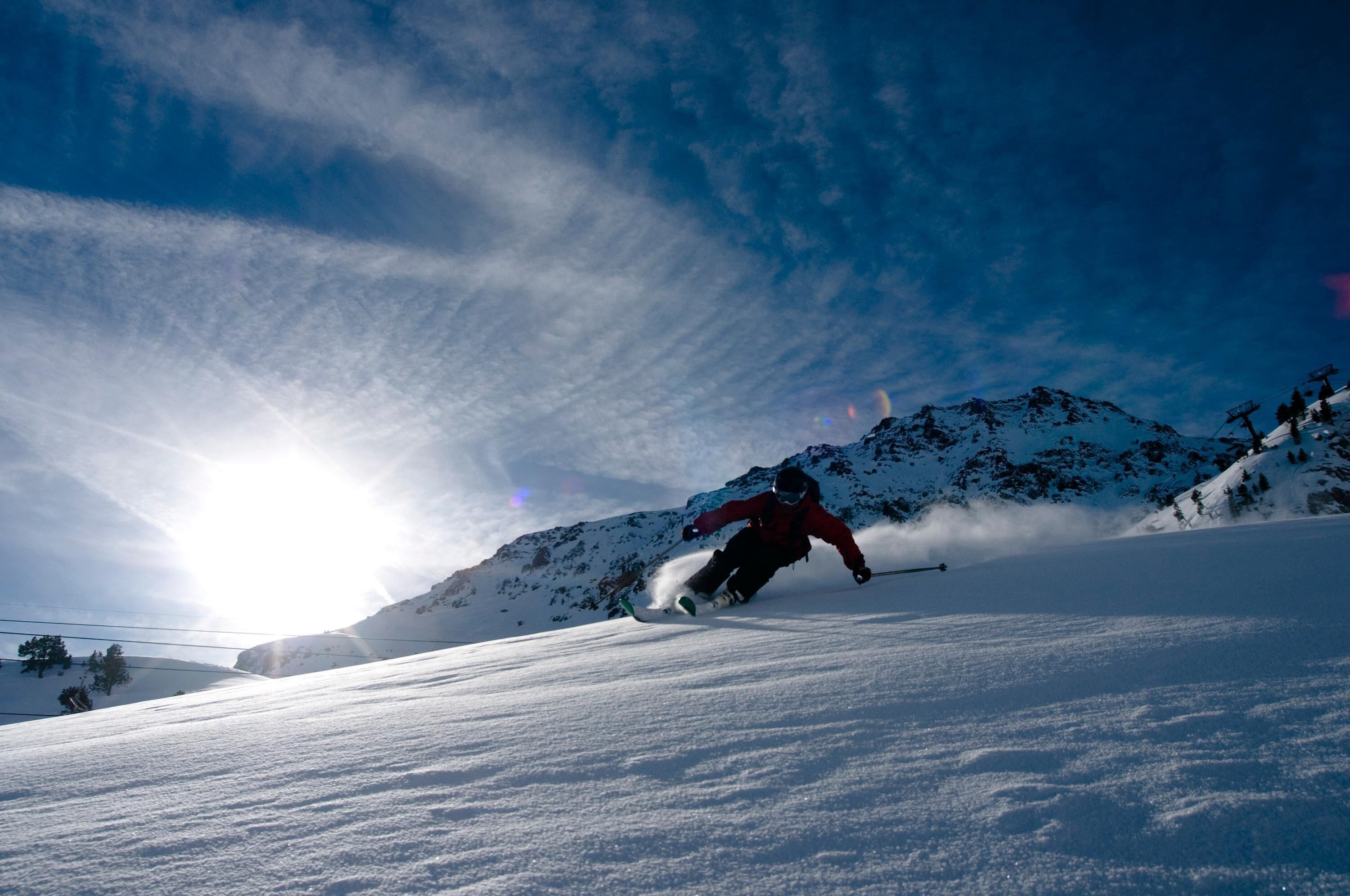 Un skieur sur une pente enneigée, sous un ciel dégagé et ensoleillé.