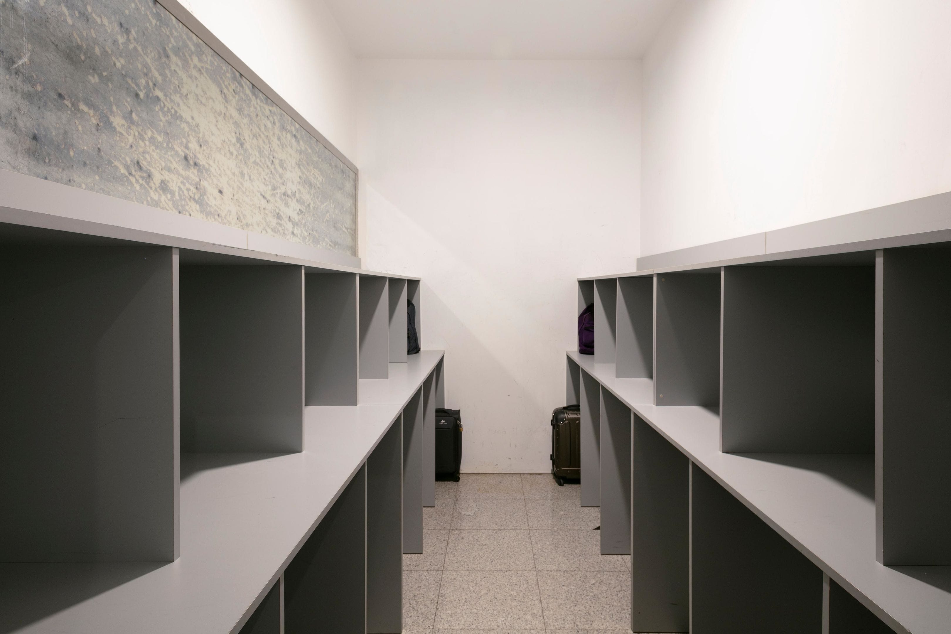 A modern, minimalist hotel room with a clean, white interior, grey shelving units, and a tiled floor.