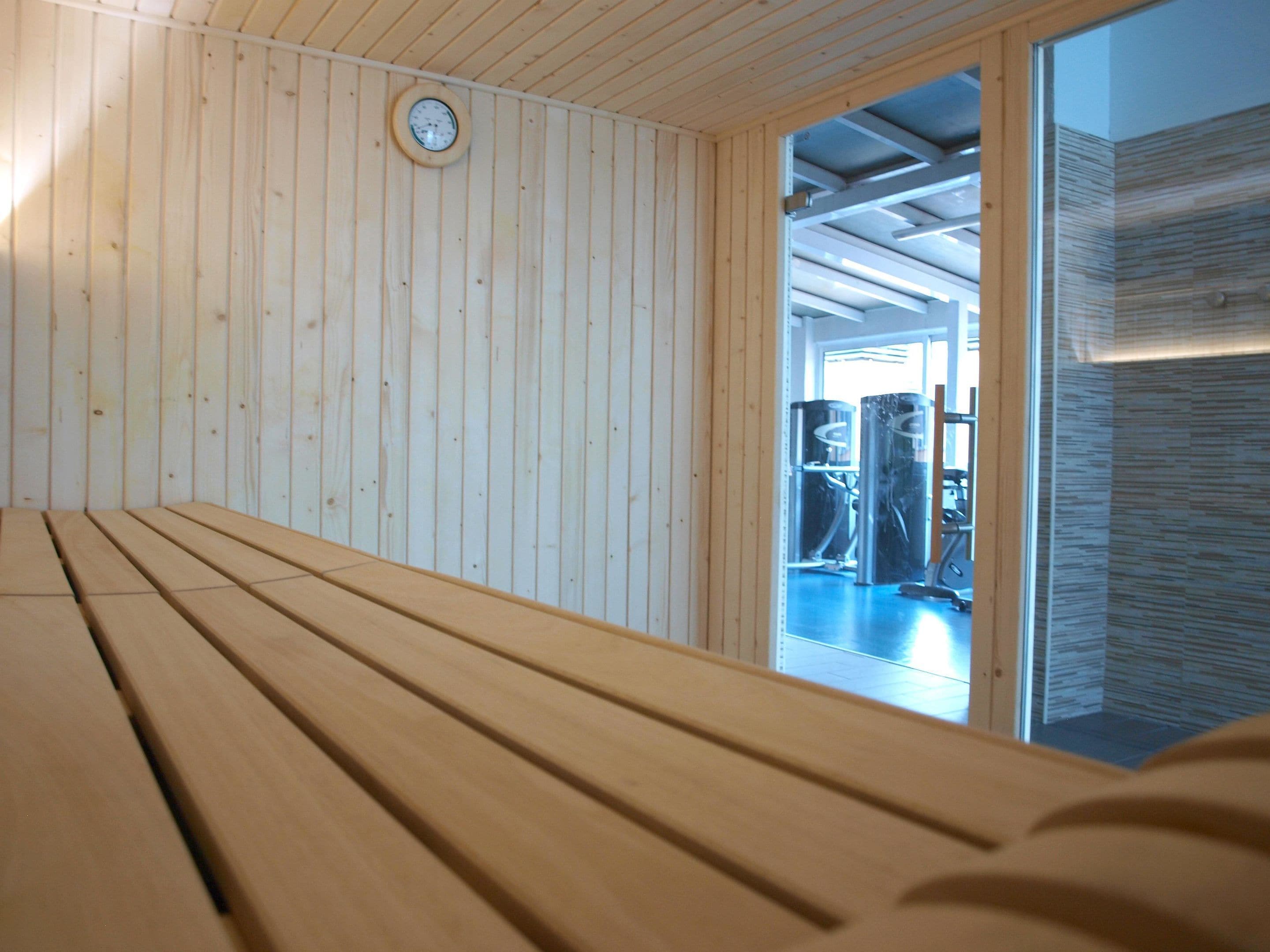 A wooden bench in a room with vertical wooden paneling and a visible door leading to another area with exercise equipment.