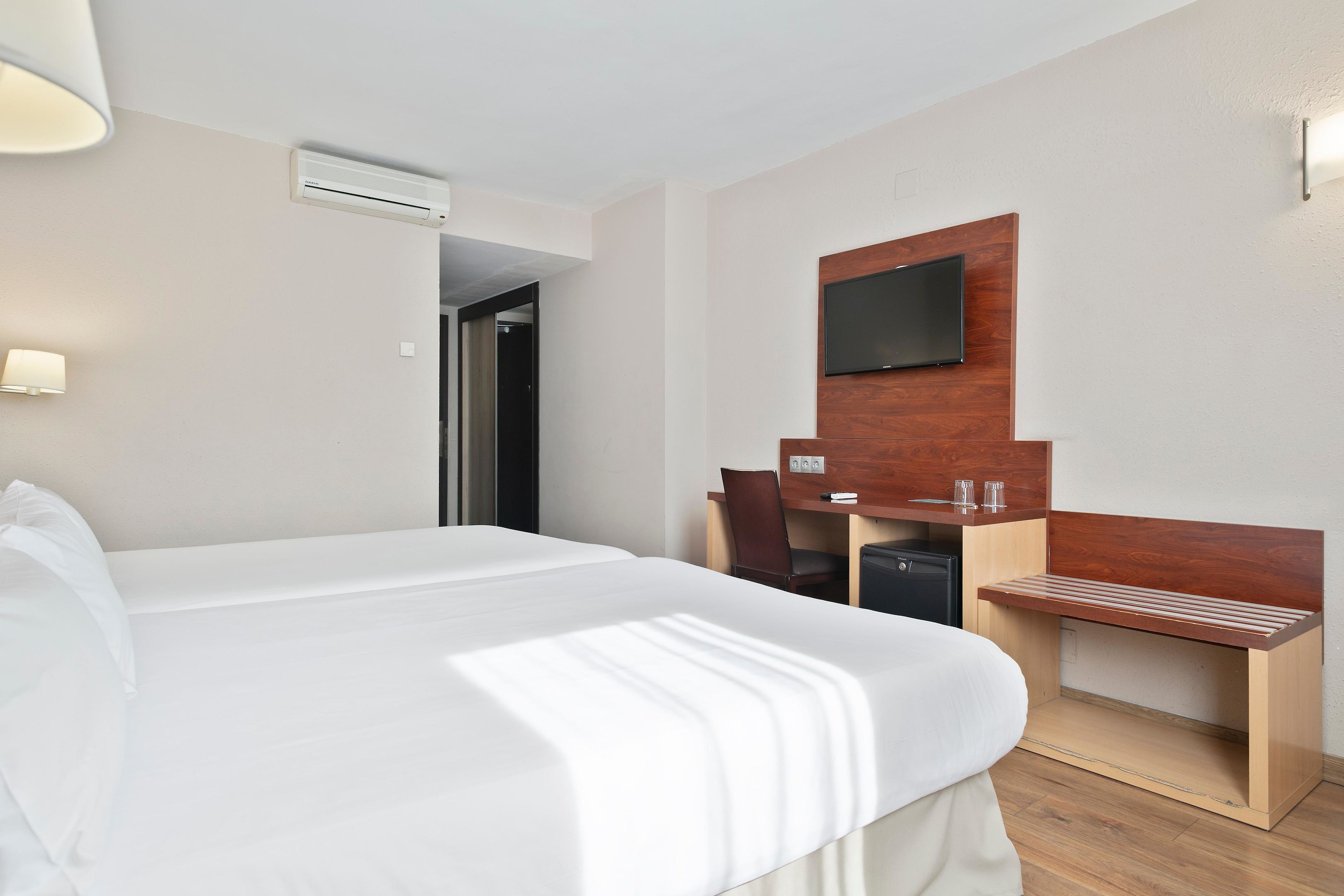Habitación de hotel con una cama grande, un escritorio de madera, un televisor montado en la pared y una pequeña zona de estar.