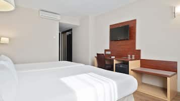 Habitación de hotel con una cama grande, un escritorio de madera, un televisor montado en la pared y una pequeña zona de estar.