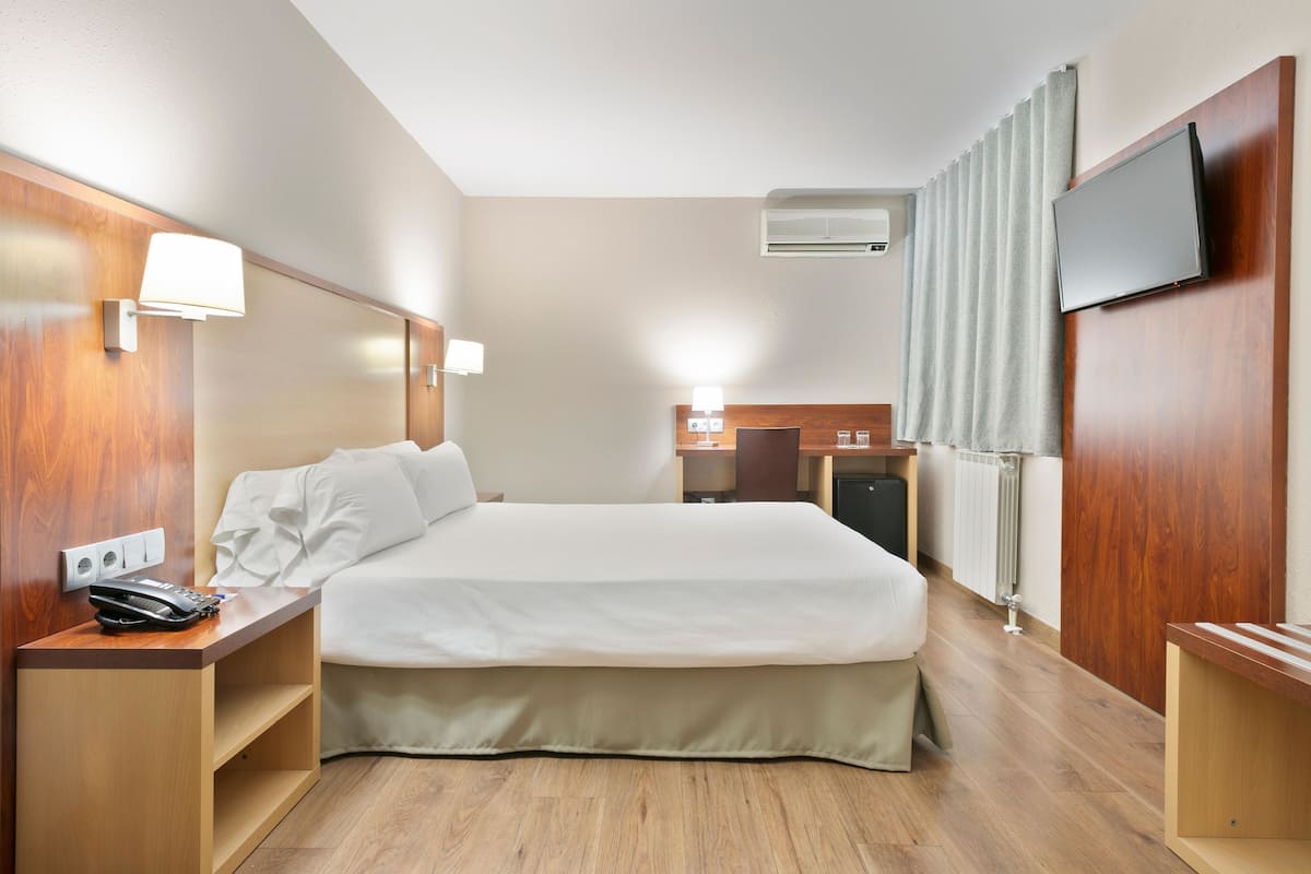 Habitación de hotel con cama, mesitas de noche, televisión y aire acondicionado.