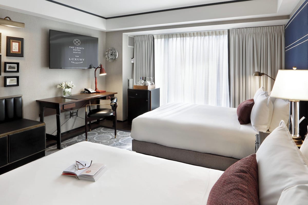 Habitación de hotel con dos camas, un escritorio, una silla, un televisor y una ventana con cortinas.
