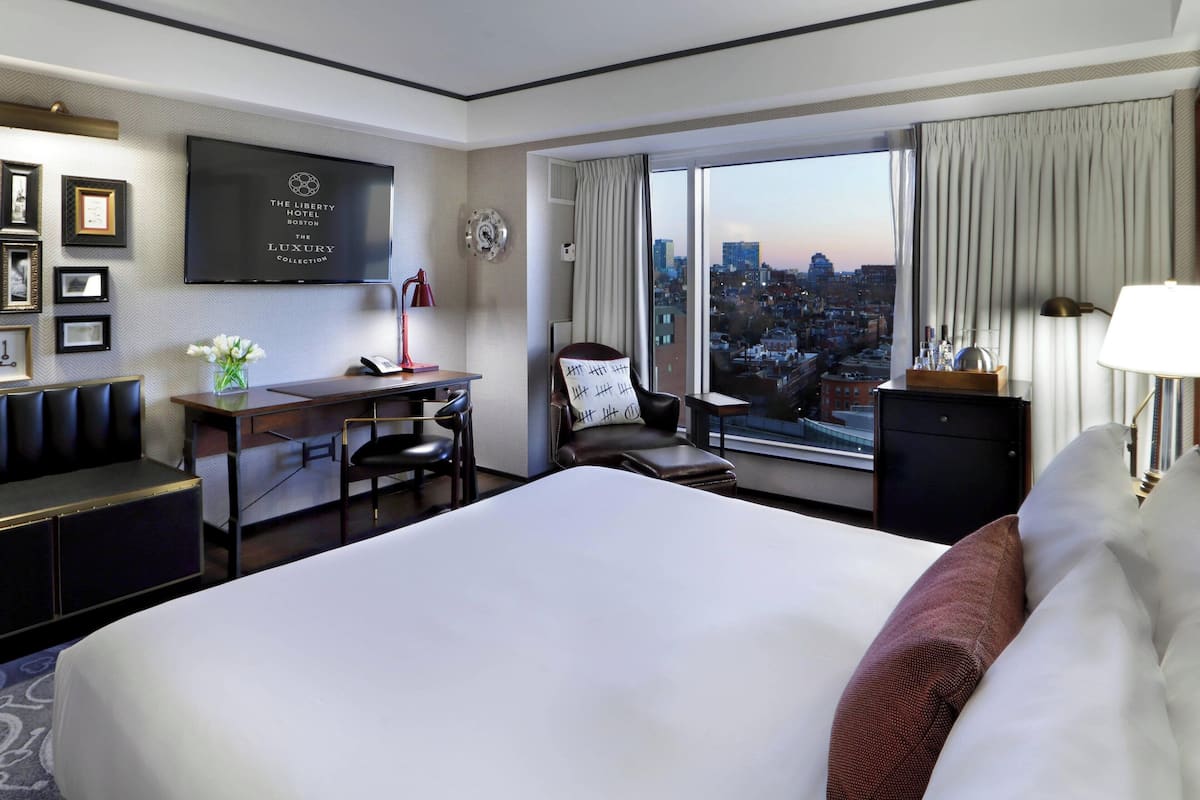 Habitación de hotel con una cama grande, un escritorio con silla, televisor montado en la pared y vistas a la ciudad a través de la ventana.