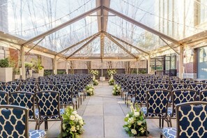A covered outdoor seating area with rows of chairs and floral arrangements.