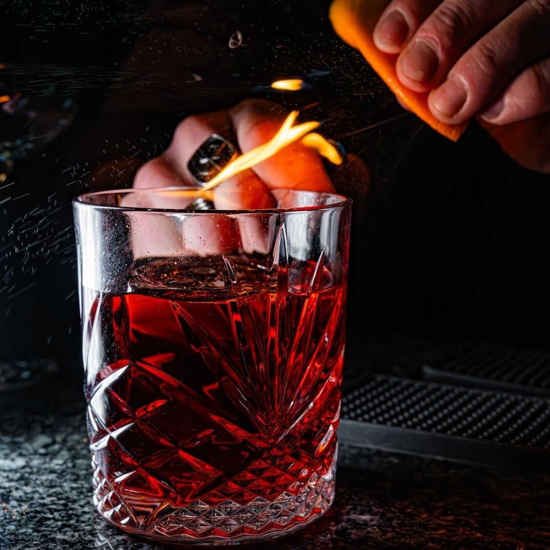A clear glass with a red liquid, possibly a cocktail, on a dark surface.